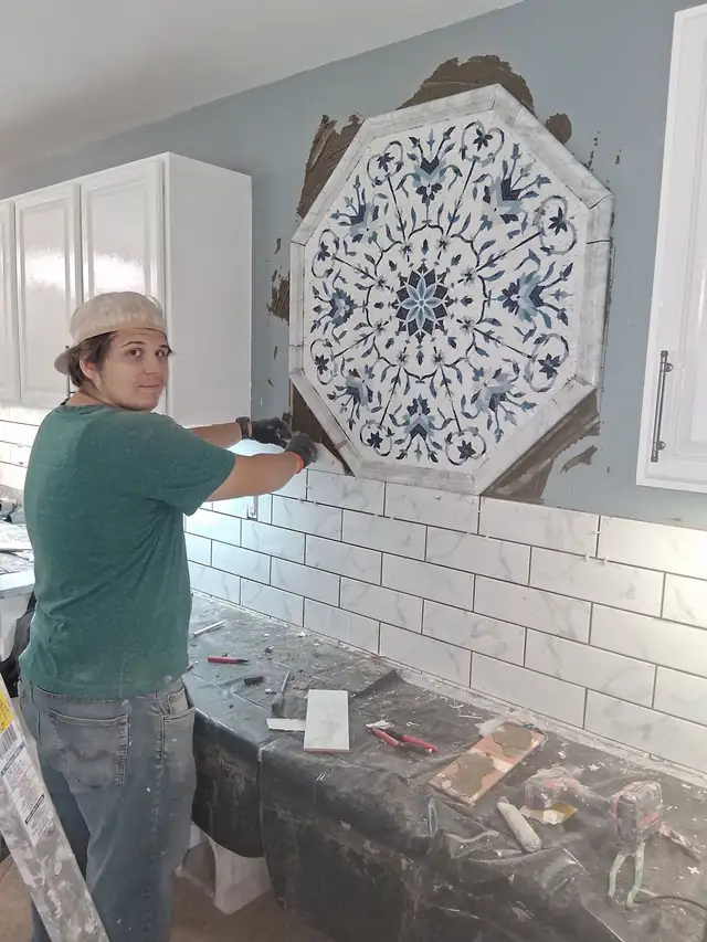 Antonio's Tile installer setting a blue and white mosaic medallion into a white subway tile wall