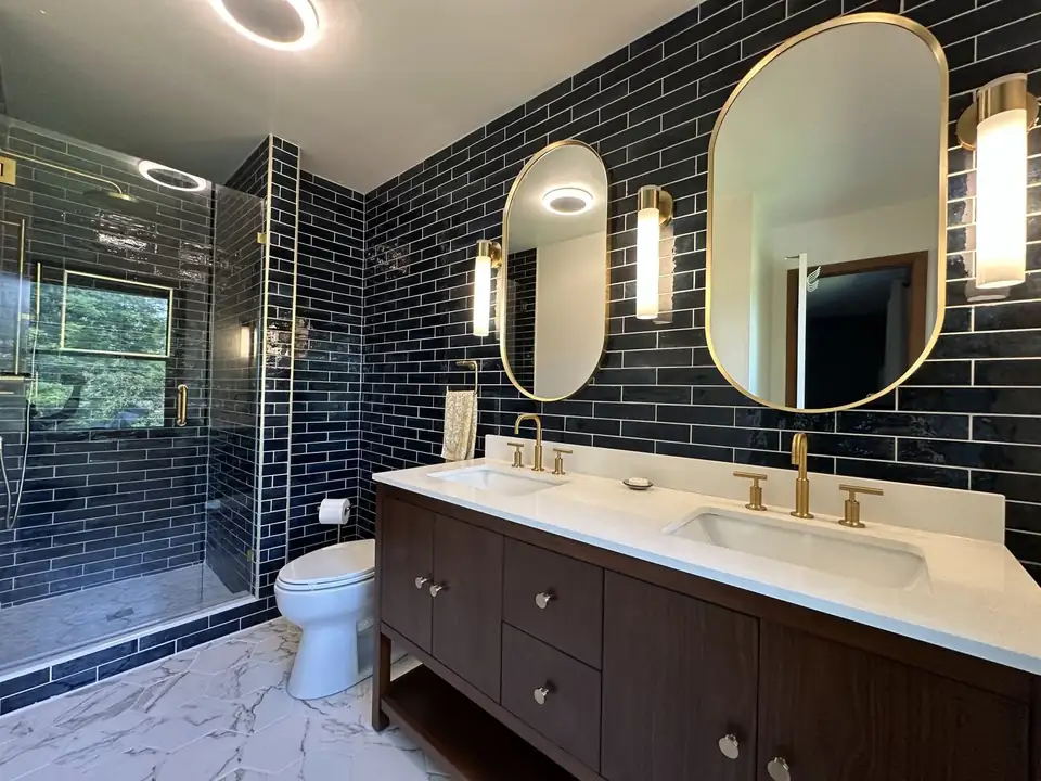 Bathroom by Antonio's Tile, Ypsilanti tile contractor: glossy navy subway tile walls, marble-look hexagon floor, walnut double vanity and brass oval mirrors