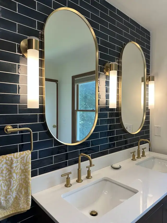 Brass oval mirrors and wall sconces on glossy navy subway tile above a white double vanity