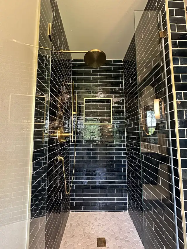 Walk-in shower in glossy navy subway tile with a recessed niche, brass shower head and frameless glass