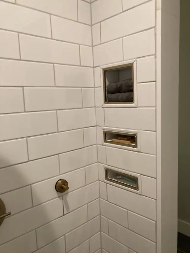 White subway tile shower wall with three recessed niches trimmed in brass
