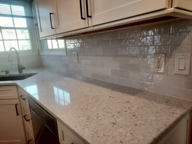 Glossy subway tile backsplash above a speckled stone countertop and white cabinets