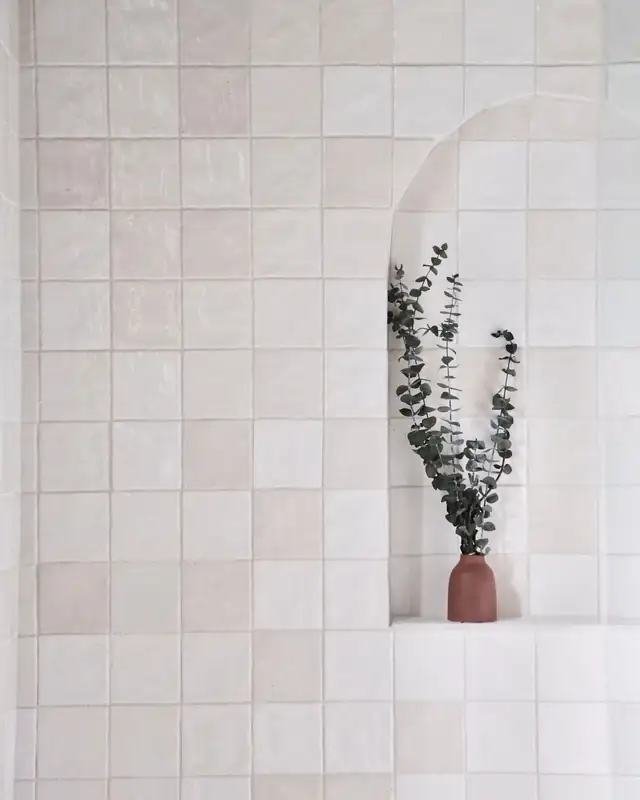 White square wall tile with a built-in ledge holding a vase of eucalyptus